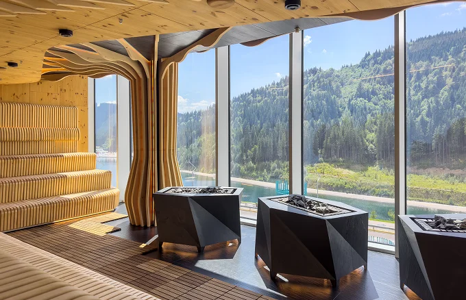 Modern houten sauna-interieur met grote panoramische ramen met uitzicht op een bos- en rivierlandschap.